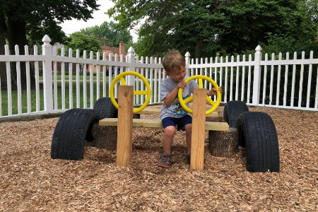 a play car made from lumber and tires. A boy plays with the steering wheel.