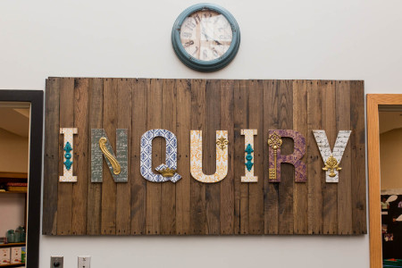 the word Inquiry made from letters of differing patters mounted to wood slats on a wall