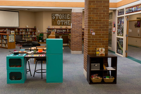 a view of the play kitchen from the front with two oven doors and a refrigerator. The rest of the library is in the background.