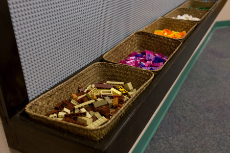 close up of different legos sorted by color in wicker baskets under the Lego wall
