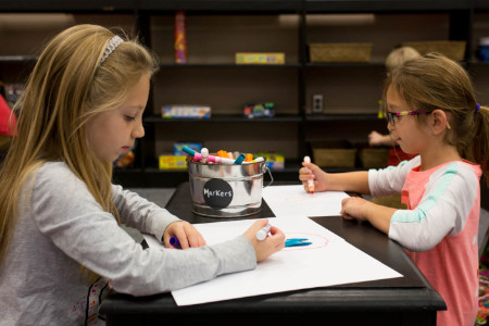 two girls writing with markers at a low table