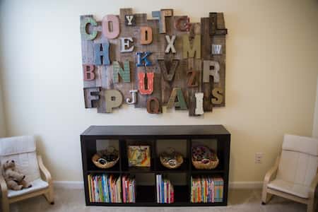 letters of various materials and styles mounted to a wall with a small bookcase underneath and two soft chairs to either side.