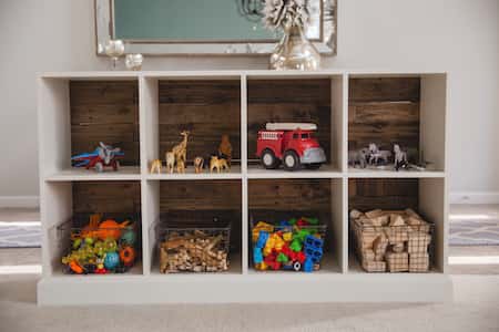 shelves with neatly arranged play objects, such as a fire truck, and airplane, small plastic animals, and various blocks in baskets.