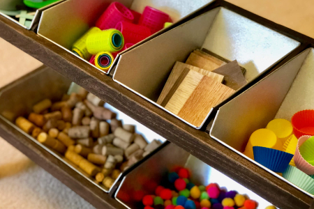 a close up of various materials in metal baskets, including hair curlers, blocks, corks, and pom poms.