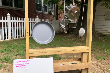 a sign next to some pots and pans hanging from an outdoor wooden structure. The sign describes the developmental skills the play station meets.